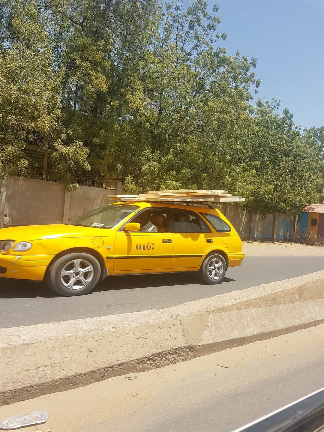 Un taxi jaune de la ville dans une rue bordée d'arbres à N'Djamena